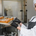 Cocinera con gorro blanco mete una bandeja en un horno industrial
