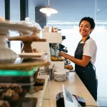Camarera joven sonríe mientras haceun café en una cafetería